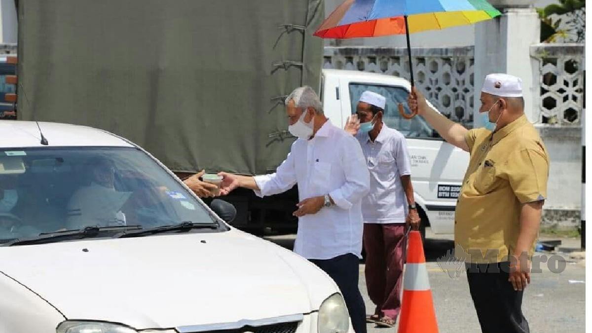 OSMAN (kiri) mengagihkan bubur lambuk kepada pemandu kenderaan di pekarangan Masjid Negeri, Kuala Terengganu, hari ini. FOTO BAHAROM BAKAR.